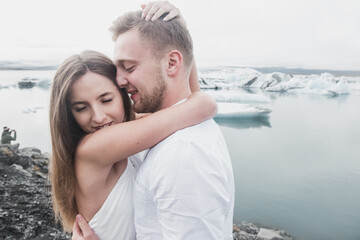 Wedding in Iceland. A guy and a girl in a white dress  are hugging while standing on a blue ice floe on a background of mountains