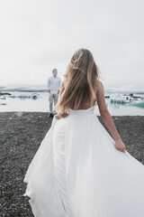 Fototapeta na wymiar Wedding in Iceland. A guy and a girl in a white dress are hugging while standing on a blue ice floe on a background of mountains