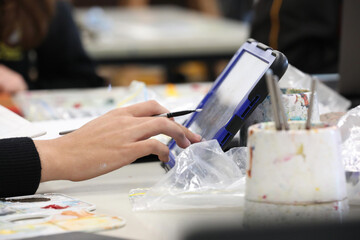 The modern visual art student in the classroom studio painting and using a digital online device...