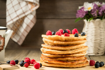 Stack of pancakes with berries on a wooden table in a rustic style