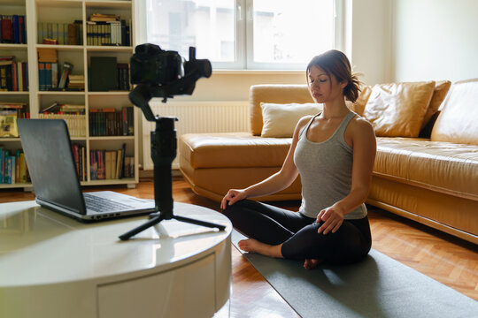 The new normal concept - adult caucasian woman meditation at home teaching yoga class in front of the camera and laptop - remote working during the covid-19 pandemic crisis - blogger work from home
