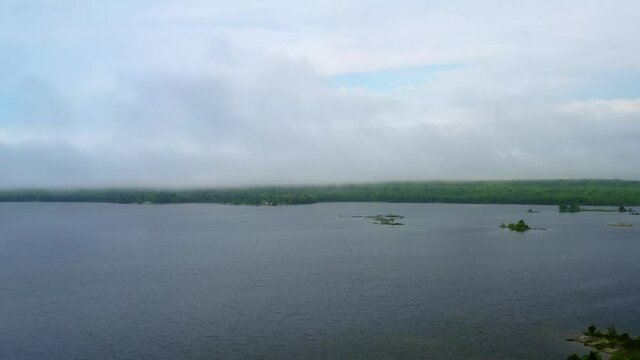 Aerial shot over a lake on a misty cloudy morning with island in the distance