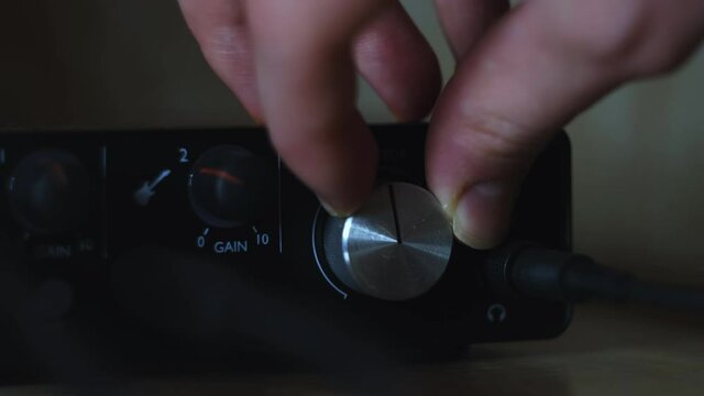 Hand adjust volume controller of the audio interface for home recording. Concept. Close up of external sound card on blurred background.