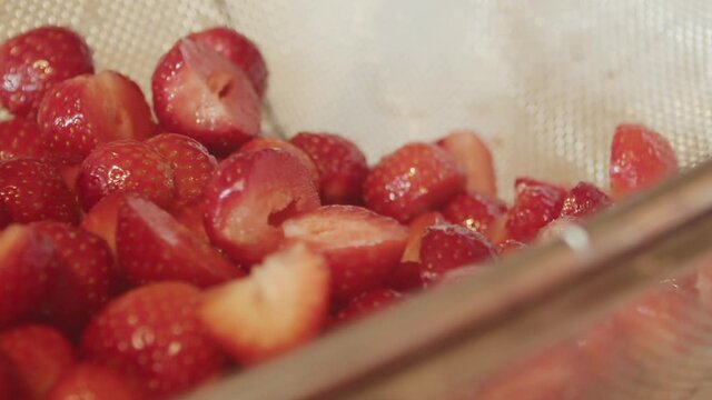 Fresh sliced strawberries in strainer basket as hand reaches inside, close-up