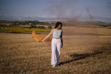 Horizontal shot of a female posing with a smoke bomb on a background of fields and windmills