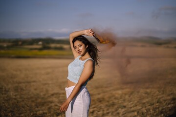 Horizontal shot of a female posing with a smoke bomb on a background of fields and windmills