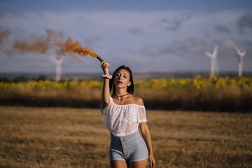 Horizontal shot of a female posing with a smoke bomb on a background of fields and windmills