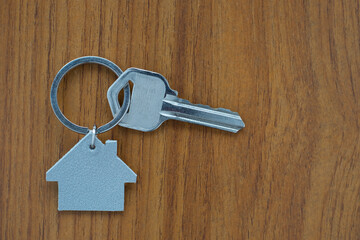 Silver key house with house shaped keychain on wooden table background. Real estate concept for buying a new home with copy space.