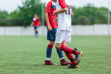 Boys in white and red sportswear plays football on field, dribbles ball. Young soccer players with ball on green grass. Training, football, active lifestyle for kids	