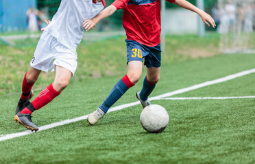 Boys in white and red sportswear plays football on field, dribbles ball. Young soccer players with ball on green grass. Training, football, active lifestyle for kids	