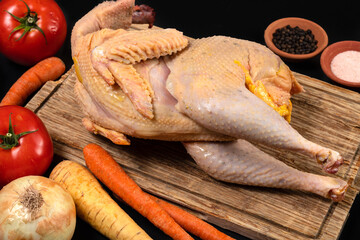 Free range farm chicken with tomatoes, onion, carrots, parsnip, and black pepper and salt lies on a rustic wood board. Fresh raw chicken and vegetables prepared for chicken soup cooking. © VIS Fine Arts