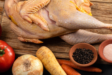 Free-range farm chicken with tomatoes, onion, carrots, parsnip, and black pepper and salt lies on a rustic wood board. Fresh raw chicken and vegetables prepared for chicken soup cooking. © VIS Fine Arts