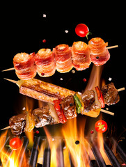 Skewers of meat, chicken with bacon and cheese falling on the burning grill and flames of fire.