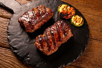 Grilled sliced beef steak on cutting board on black board over wooden table.