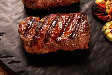 Grilled sliced beef steak on cutting board on black board over wooden table.
