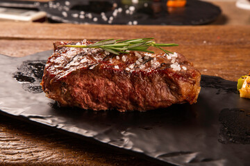 Grilled sliced beef steak on cutting board on black board over wooden table.