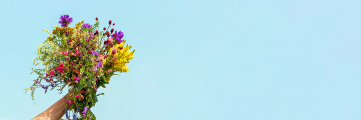 Female hand holds bright colorful bouquet of wild flowers against blue sky. Womens day, Mothers...