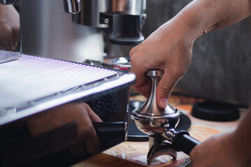 Close-up view of on hands barista presses ground coffee using tamper.