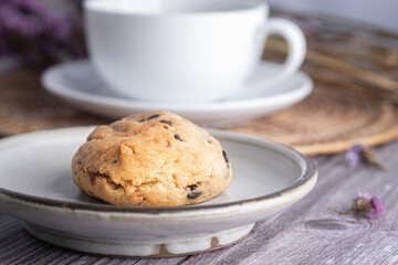 Close-up of a cookie on a plate with a white coffee cup and flower blurred background.