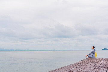 Fototapeta na wymiar a man in a gray tracksuit sits on the edge of a pier in Thailand and practices meditation, a person retired from the bustle of the city in search of truth
