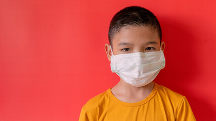 A boy in Thailand wears a COVID-19 virus mask and the dust is watching. Interior red wall background, New Normal