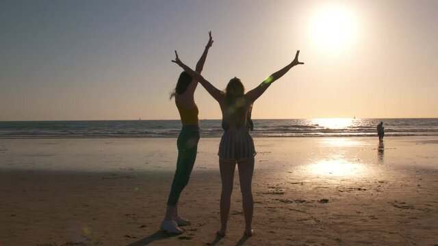 Two young women frolic at the sea shore at sunset