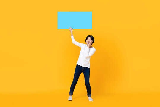 Shocked young beautiful millennial Asian woman holding blue speech bubble with blank space for text isolated on colorful yellow background