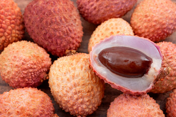 Chinese fruits and oriental foods concept with picture of one lychee fruit peeling the bumpy skin to expose the juicy delicate pulp on top of many lychees with copy space