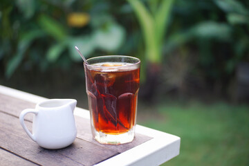 Clsoe up of a glass of iced tea with blurry garden background.