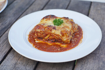 Close up of meat lasagna on a white plate with wooden table background.