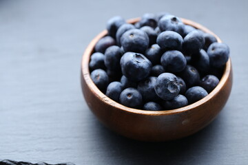  Blueberry berry in a wooden round cup close-up on a black slate background.Healthy bio  dessert and snack.Vegetarian and vegan food. blueberries season.