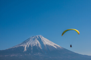 Fototapeta na wymiar 青空の中で富士山に向かって飛ぶ黄色いパラグライダー　冬　2月