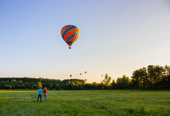 Kyiv, Ukraine - 06/26/2020: Hot air balloons in clear sky over field with people. Colorful balloons on aerial landscape background. Summer leisure. Hot air balloon in flight in the morning.