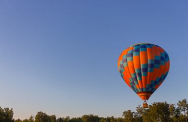Kyiv, Ukraine - 06/26/2020: Hot air balloon in clear summer sky over trees. Colorful balloon on summer landscape background. Summer leisure. Hot air balloon in flight in the morning.