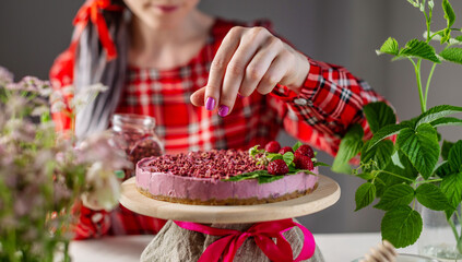 Woman is decorating with freeze dried raspberries a raw berry mousse cake. Concept of delicious and healthy summer desserts