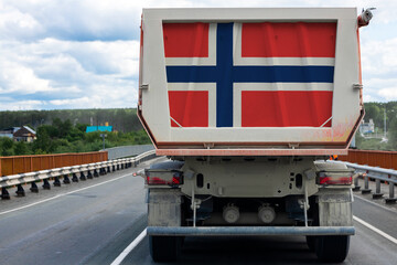 Big dirty truck with the national flag of Norway. moving on the highway, against the background of the village and forest landscape. Concept of export-import,transportation, national delivery of goods