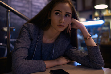 Girl in grey suit posing in cafe with smartphone