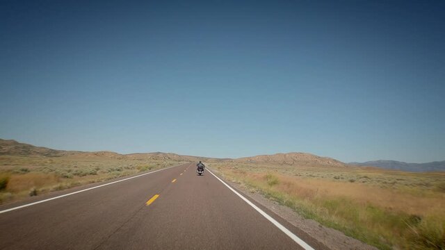 Riding along an endless highway in the US in the desert sun with blue sky filmed from the bike behind