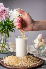 Hand is pouring rice grains into a glass of natural rice milk. Alternative vegetarian drink for a healthy diet