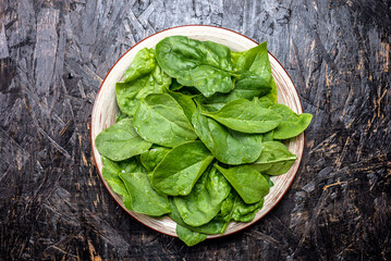Green leaves of fresh spinach in a plate on a dark background. Healthy vegetarian food. Top view