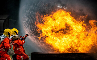 Two brave firefighter in fire suit on rescue duty using water from hose extinguishing fighting with...