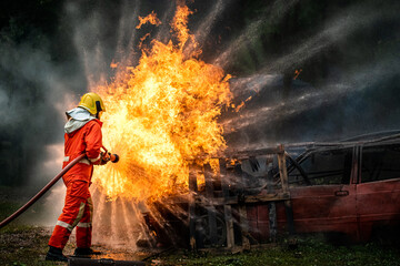 Brave firefighter in fire suit on rescue duty using water from hose extinguishing fighting with big...