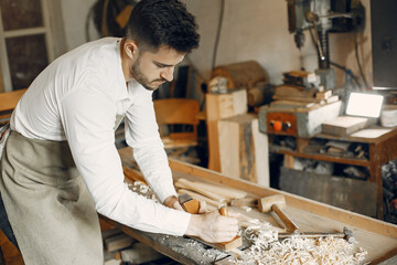 Man working with a wood. Carpenter in a white shirt. Man with a chisel