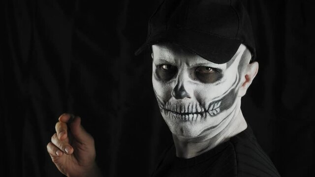 Man with make-up skeleton and black cap on a dark background. Halloween or horror theme. High quality 4k footage