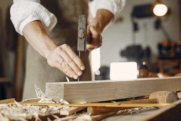 Man working with a wood. Carpenter in a white shirt. Man hammering nails into the wood