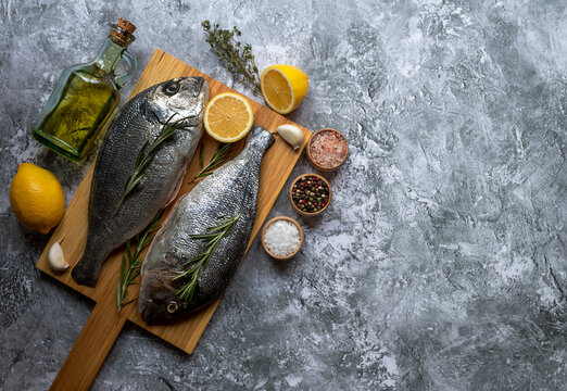 Fresh fish dorade or sea bass on cutting board with ingredients for cooking. Top view with copy space.