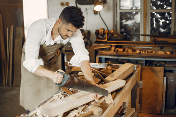 Man working with a wood. Carpenter in a white shirt. Worker with a saw