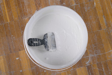 close up of a bucket with white putty for concrete walls and a spatula for applying
