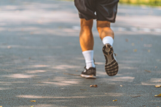 Blurred image behind Asian jogger, back side of Asian adult man's legs jogging in park on path way, wearing black shorts and sport shoes, white socks, warm tone light, space for text.