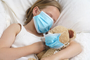 A sick teenage girl is playing with a toy wearing a protective mask.